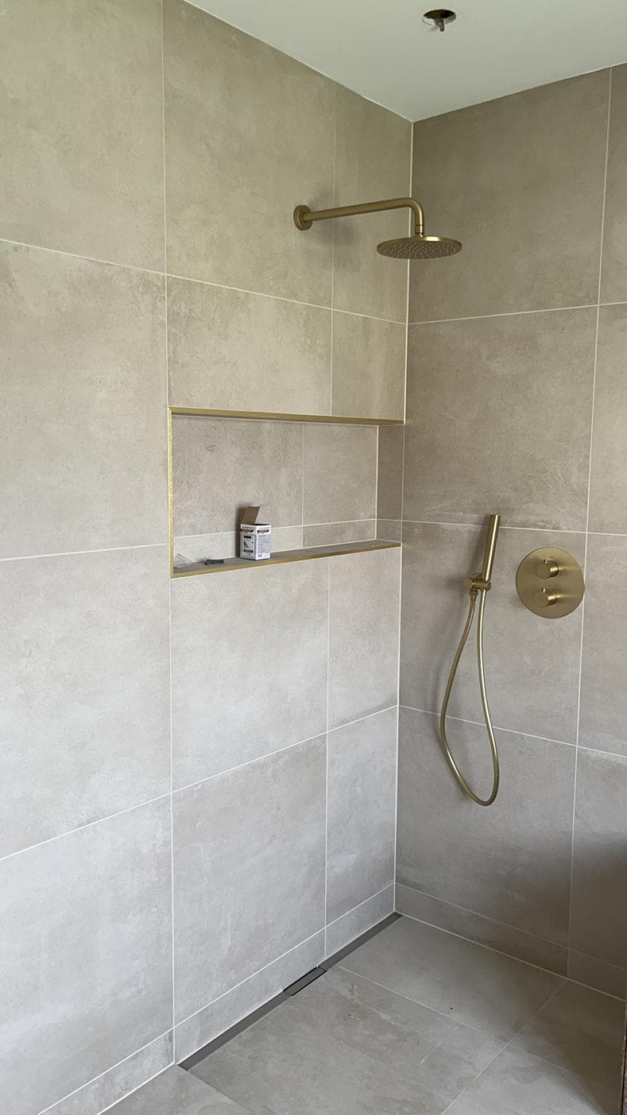 Douche à l’italienne à La Motte-Servolex : carrelage beige aspect pierre grand format, caniveau linéaire, niche à profilé doré et robinetterie encastrée or brossé