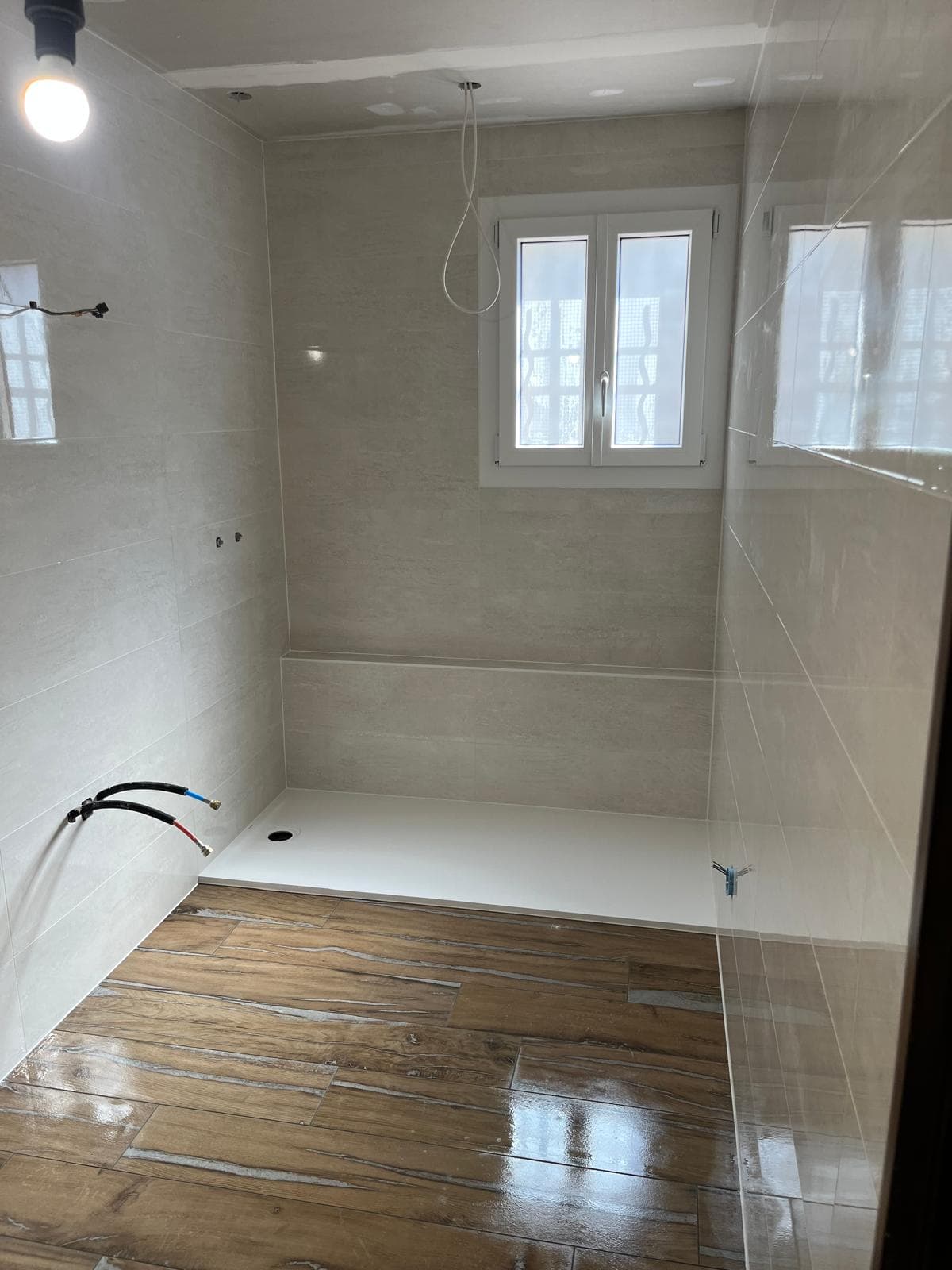 Salle de bain en finition à Albertville : faïence claire posée à l’horizontale, grand receveur extraplat blanc devant un muret carrelé et sol en grès imitation parquet