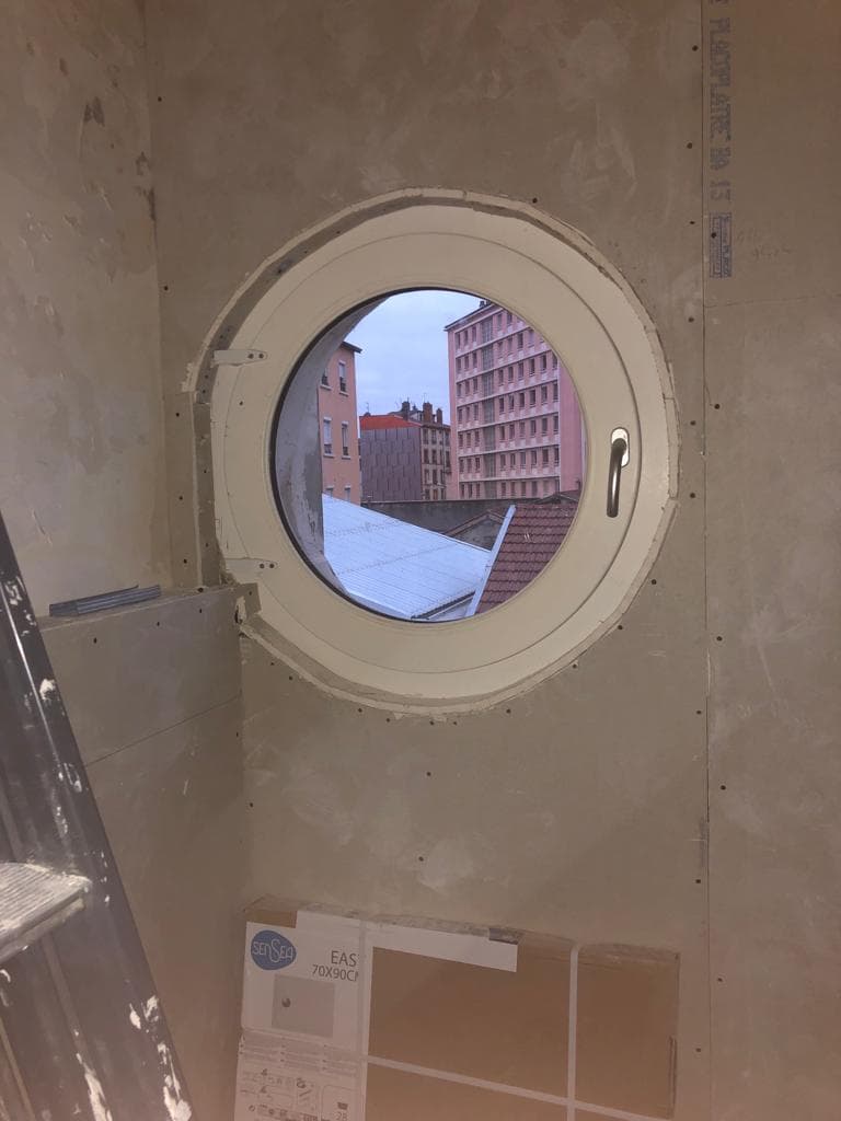 Doublage en plaques de plâtre BA13 vissées, découpé autour d’une fenêtre ronde de type hublot, avant bandes et enduit, dans un studio d’Annemasse
