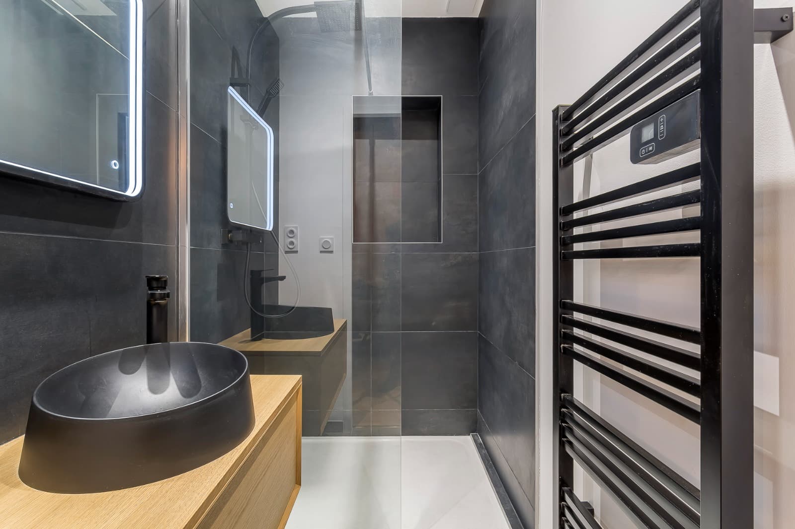 Salle de douche à Bourg-Saint-Maurice : faïence anthracite grand format, niche carrelée, receveur extraplat blanc, vasque noire sur meuble chêne et sèche-serviettes noir